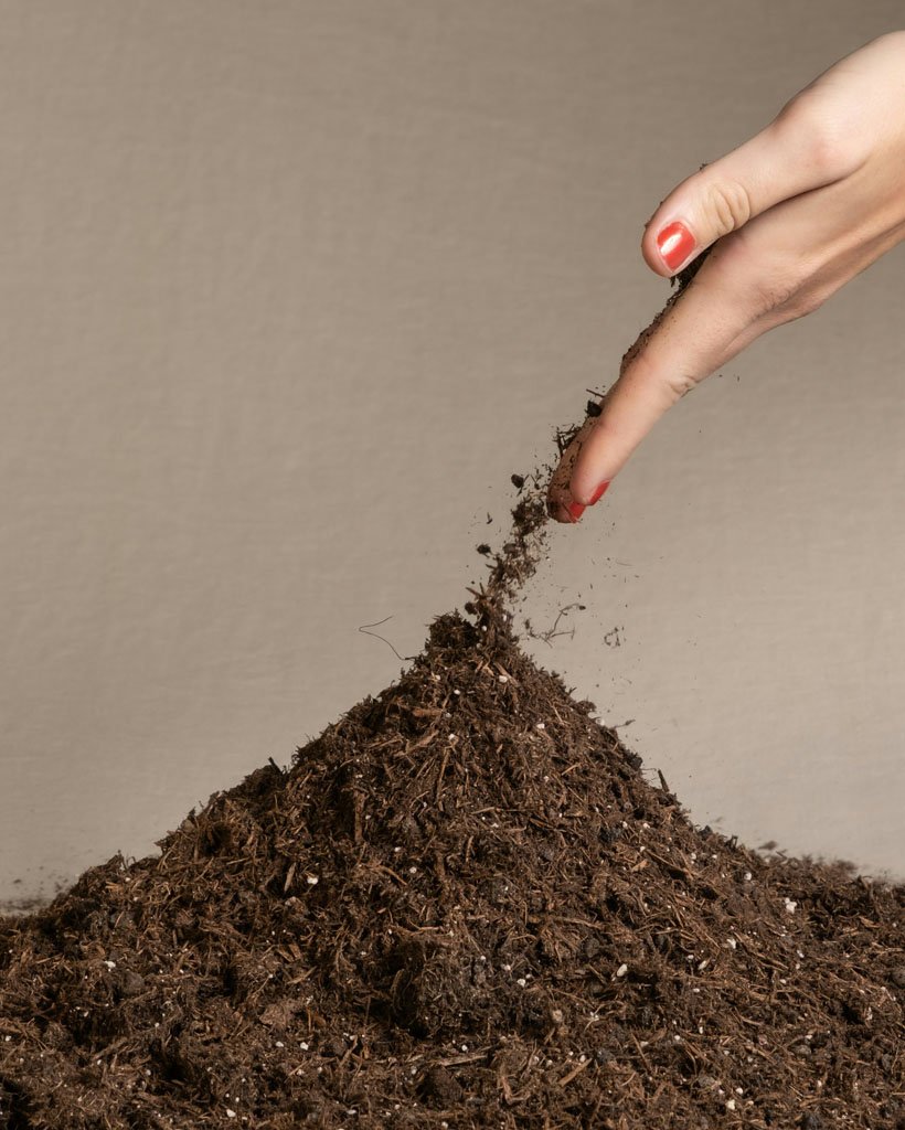 A hand releasing soil into a pile of soil. God and Garden